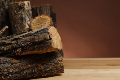 Photo of Pile of cut firewood on wooden table against brown background, closeup. Space for text