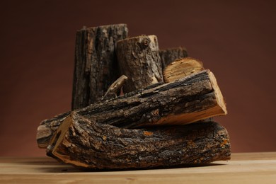 Photo of Pile of cut firewood on wooden table against brown background, closeup