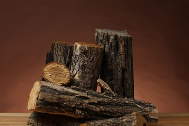 Photo of Pile of cut firewood on wooden table against brown background, closeup