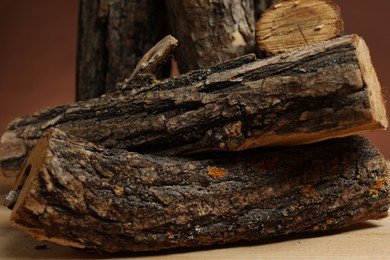 Photo of Pile of cut firewood on wooden table against brown background, closeup