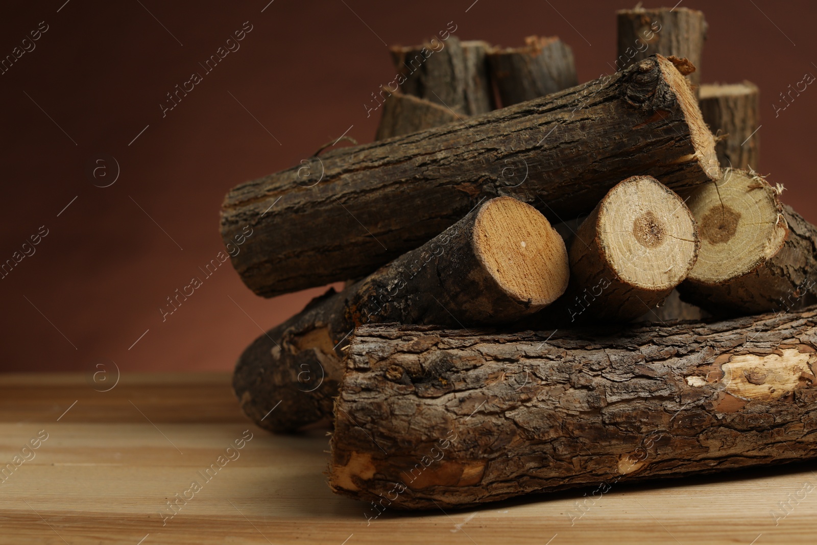 Photo of Pile of cut firewood on wooden table against brown background, closeup. Space for text