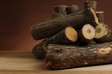 Photo of Pile of cut firewood on wooden table against brown background, closeup. Space for text