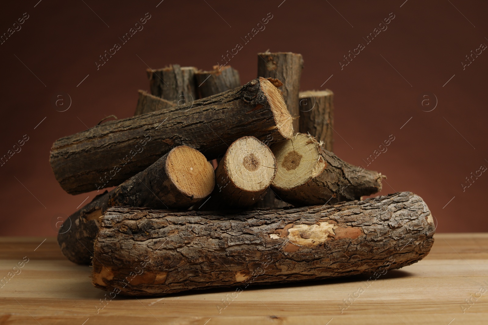 Photo of Pile of cut firewood on wooden table against brown background, closeup