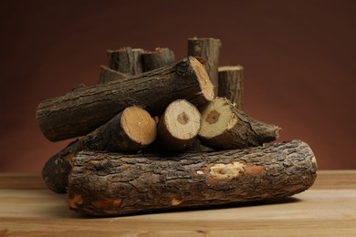 Photo of Pile of cut firewood on wooden table against brown background, closeup
