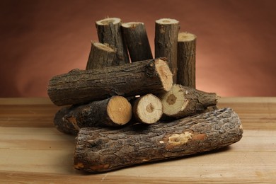 Photo of Pile of cut firewood on wooden table against brown background, closeup