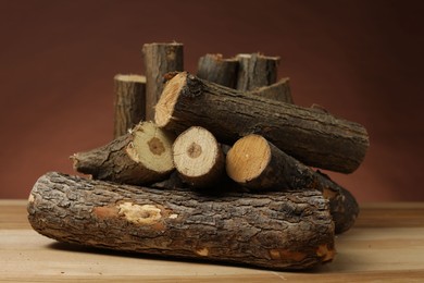 Photo of Pile of cut firewood on wooden table against brown background, closeup