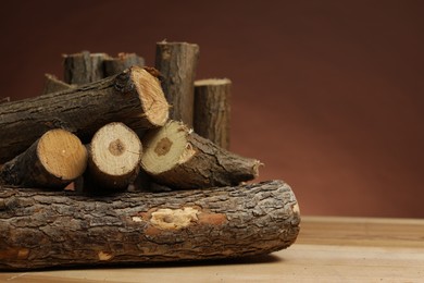 Photo of Pile of cut firewood on wooden table against brown background, closeup. Space for text