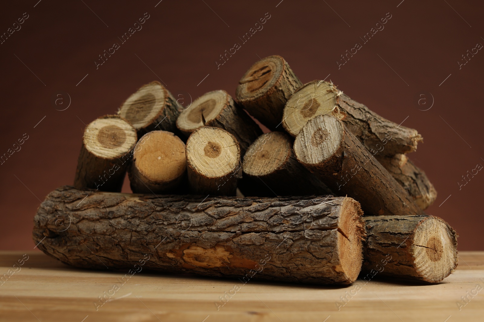 Photo of Pile of cut firewood on wooden table against brown background