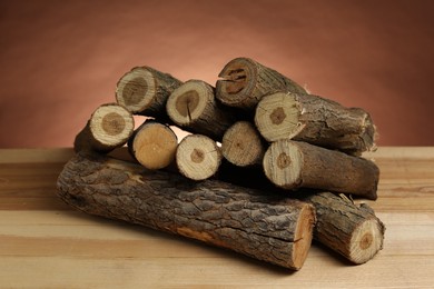 Photo of Pile of cut firewood on wooden table against brown background, closeup