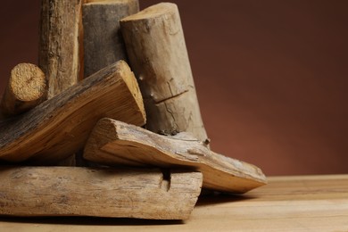 Photo of Pile of cut firewood on wooden table against brown background, closeup. Space for text
