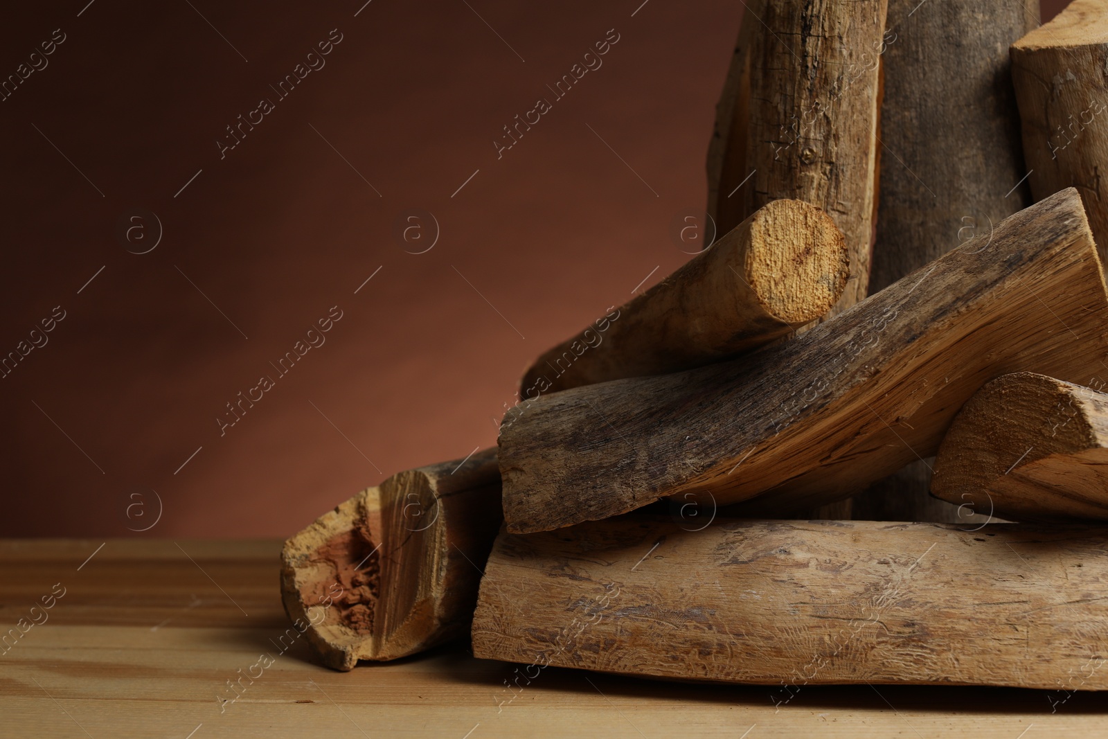 Photo of Pile of cut firewood on wooden table against brown background, closeup. Space for text