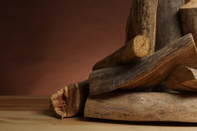 Photo of Pile of cut firewood on wooden table against brown background, closeup. Space for text