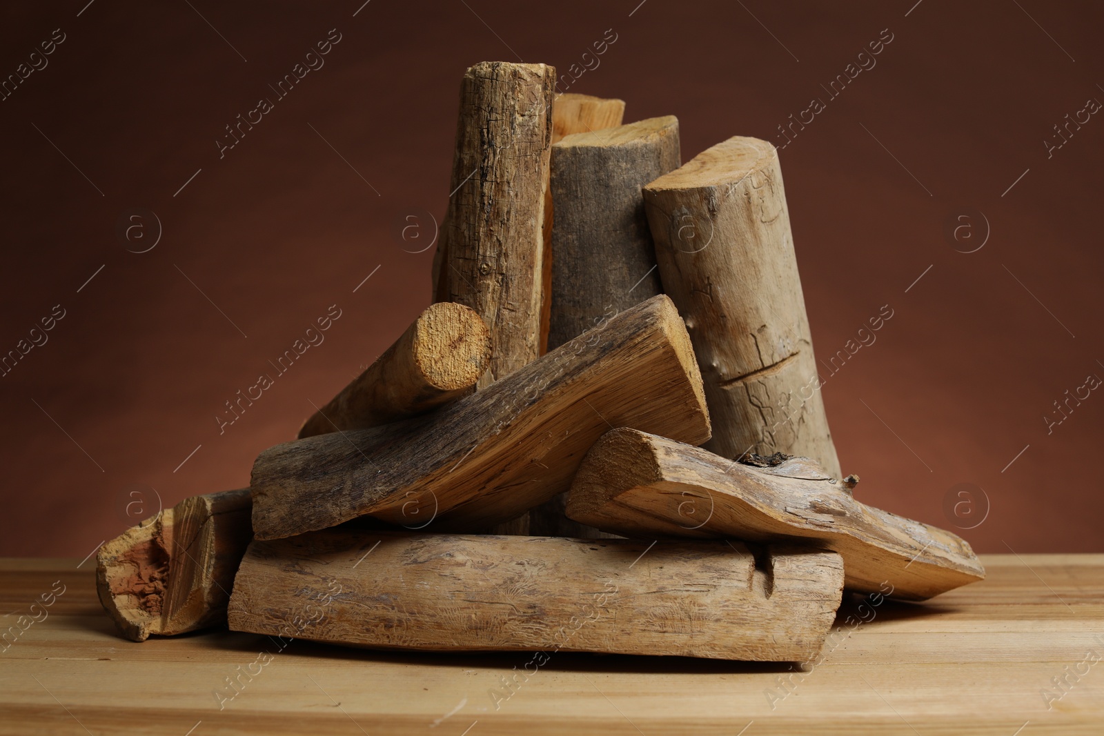 Photo of Pile of cut firewood on wooden table against brown background