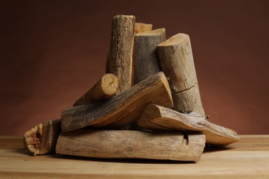 Photo of Pile of cut firewood on wooden table against brown background