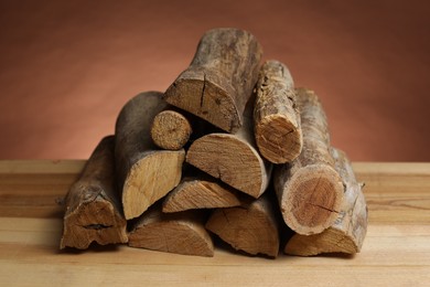 Photo of Pile of cut firewood on wooden table against brown background, closeup