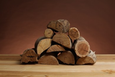 Photo of Pile of cut firewood on wooden table against brown background