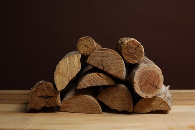 Photo of Pile of cut firewood on wooden table against brown background, closeup