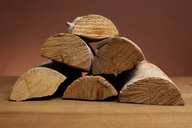 Photo of Pile of cut firewood on wooden table against brown background, closeup