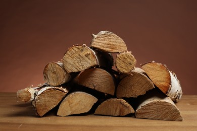 Photo of Pile of cut firewood on wooden table against brown background, closeup