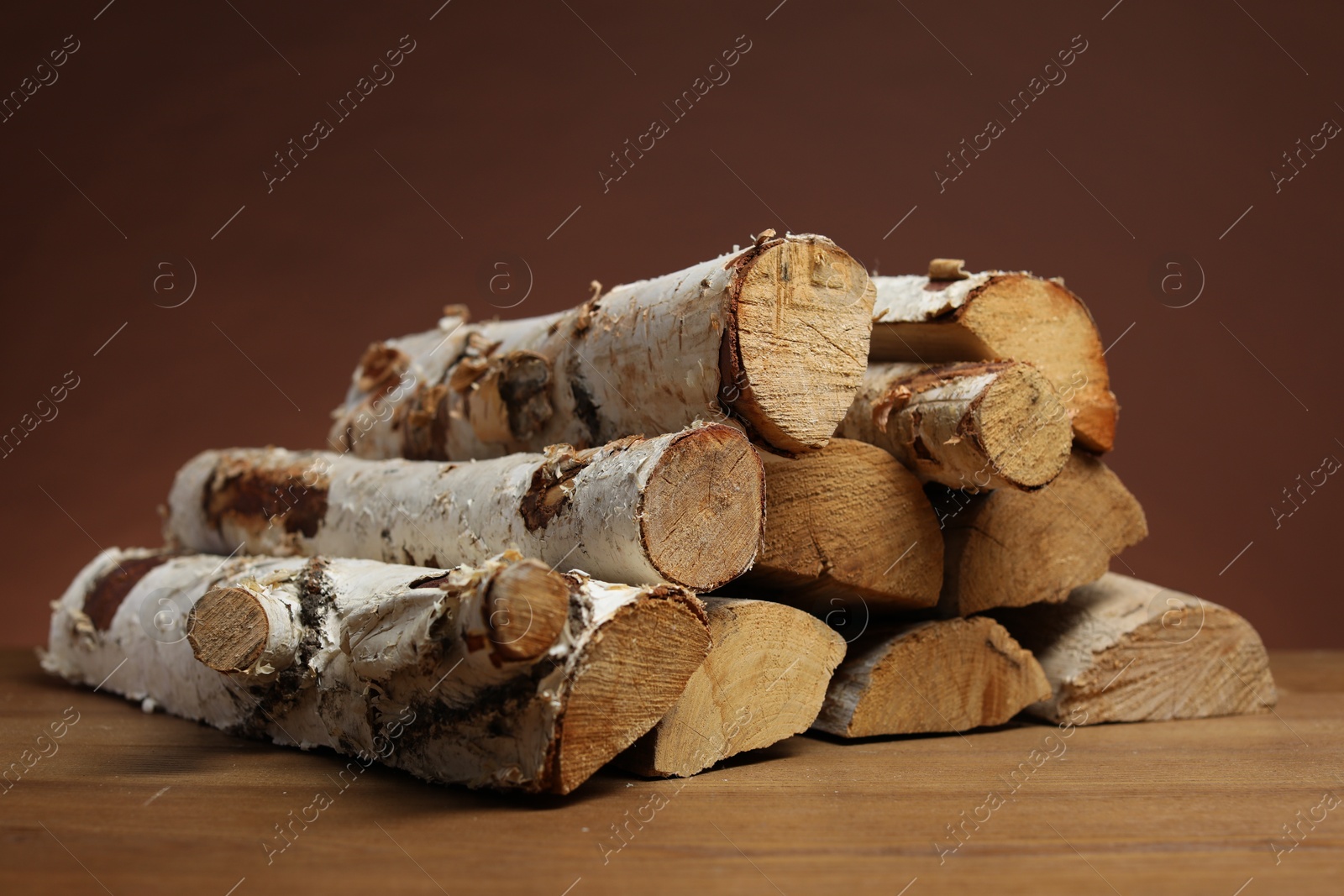 Photo of Pile of cut firewood on wooden table against brown background, closeup