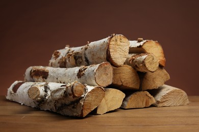 Photo of Pile of cut firewood on wooden table against brown background, closeup