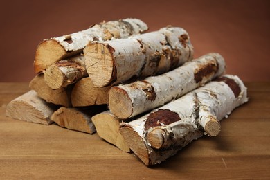 Photo of Pile of cut firewood on wooden table against brown background, closeup