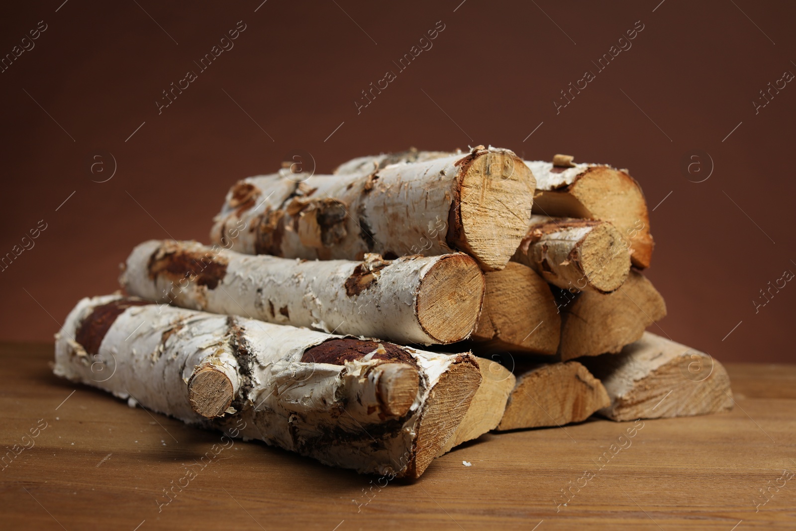 Photo of Pile of cut firewood on wooden table against brown background, closeup