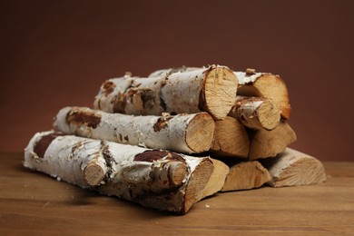 Photo of Pile of cut firewood on wooden table against brown background, closeup