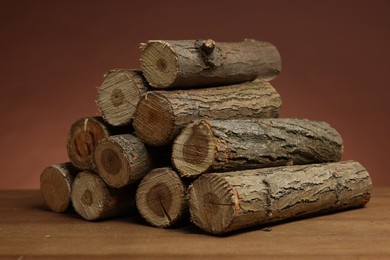 Photo of Pile of cut firewood on wooden table against brown background
