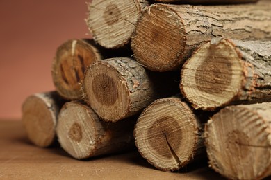 Photo of Pile of cut firewood on wooden table against brown background, closeup