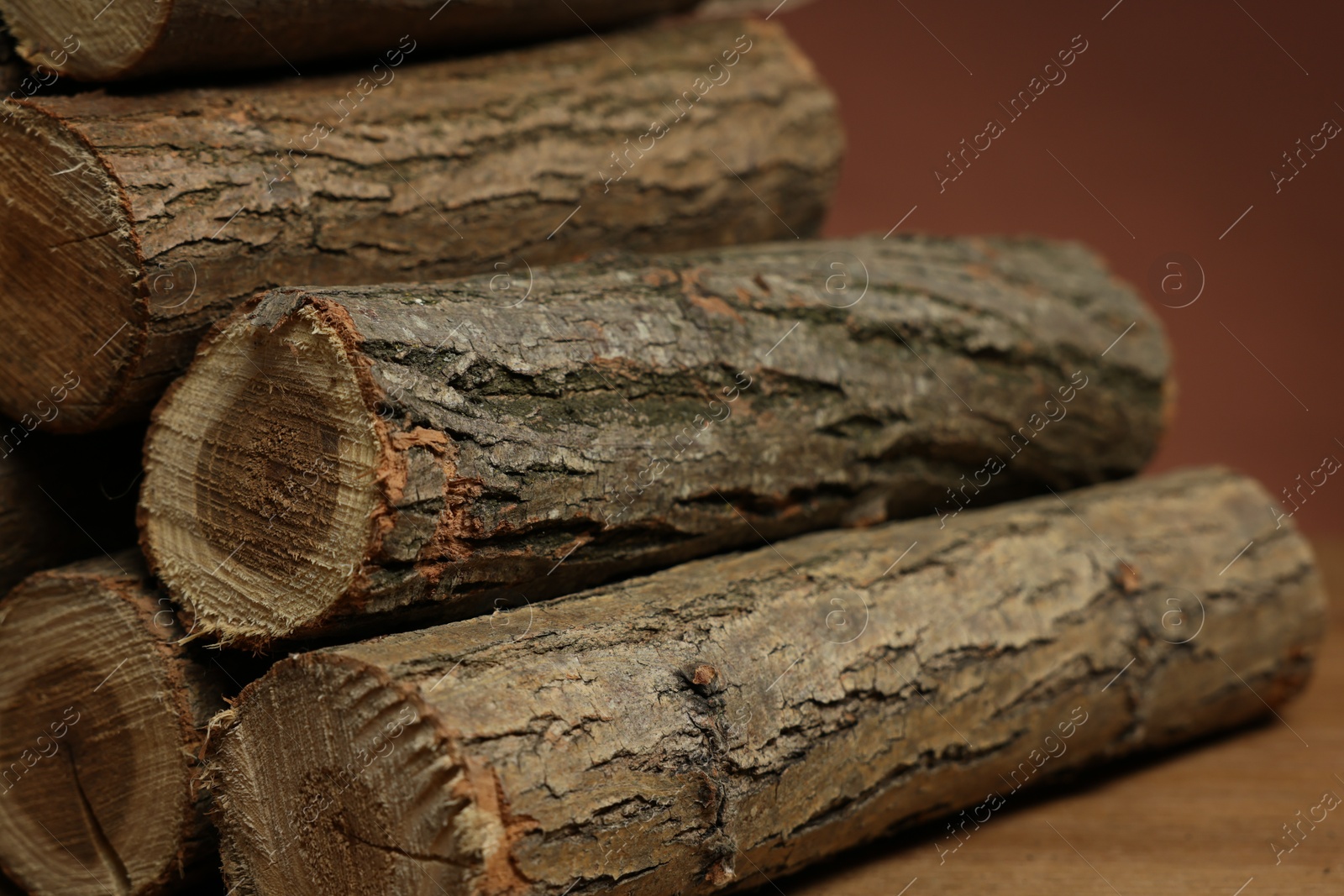 Photo of Pile of cut firewood on wooden table against brown background, closeup