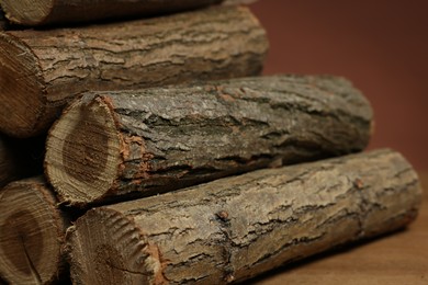Photo of Pile of cut firewood on wooden table against brown background, closeup
