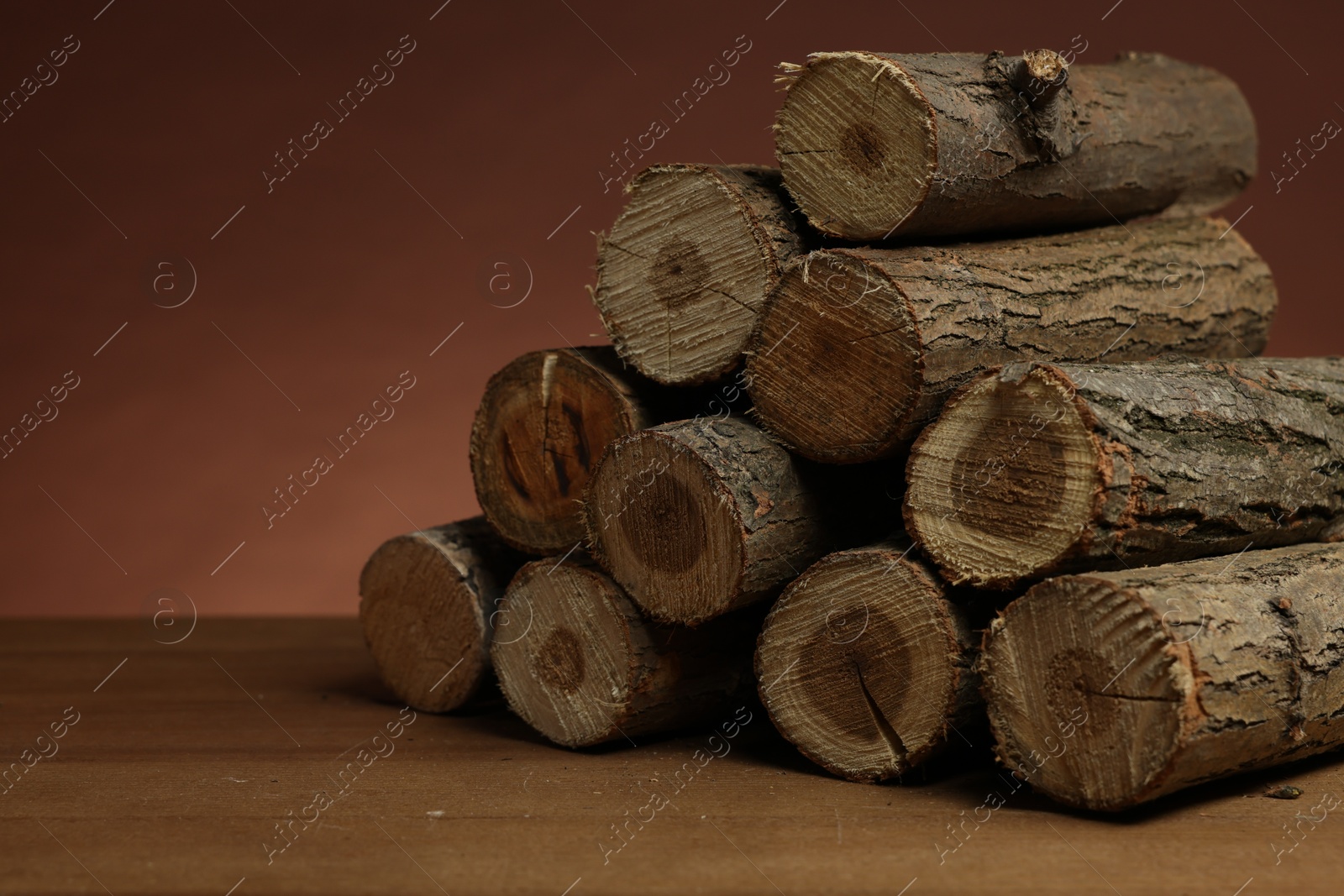 Photo of Pile of cut firewood on wooden table against brown background, closeup. Space for text
