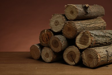 Photo of Pile of cut firewood on wooden table against brown background, closeup. Space for text