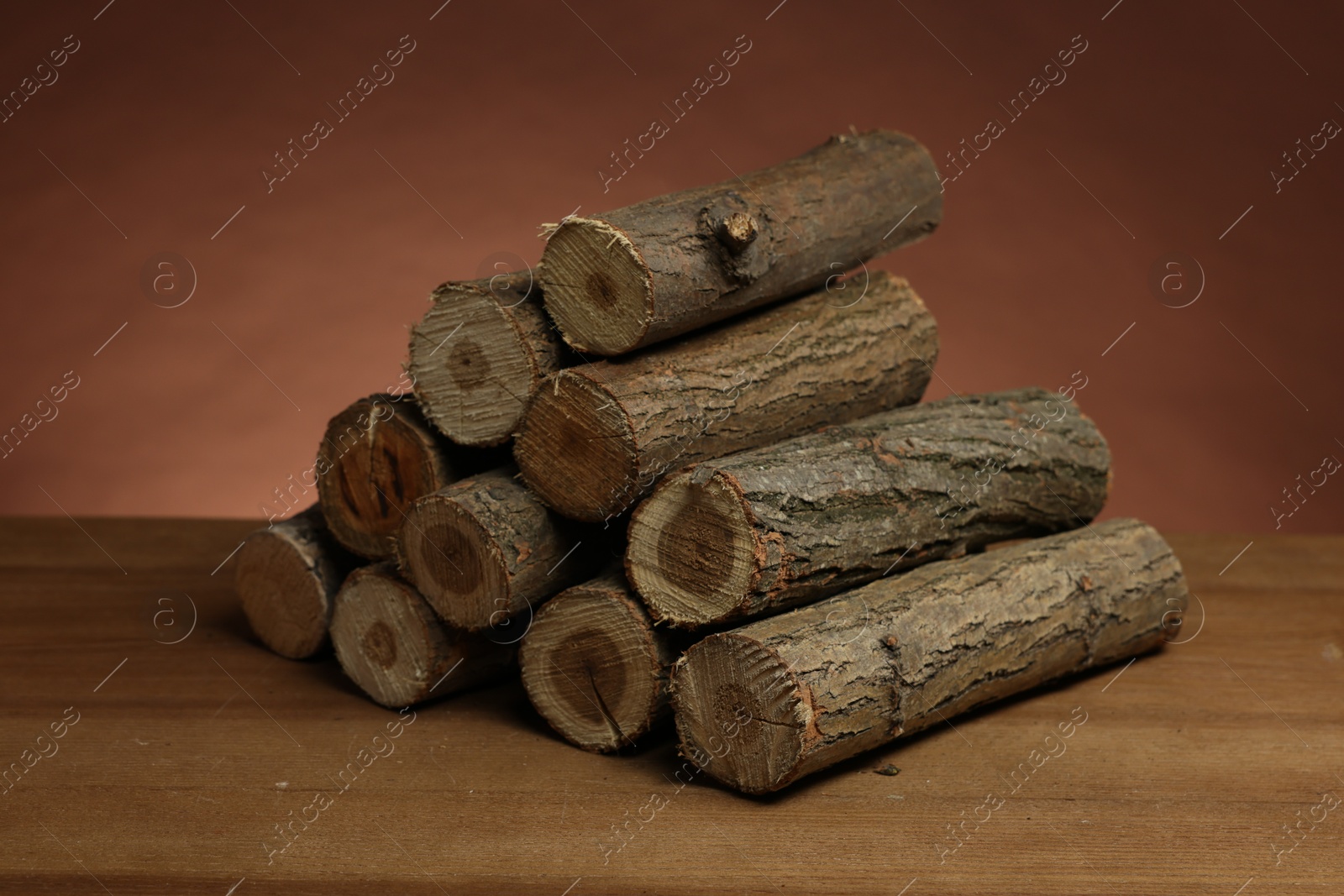Photo of Pile of cut firewood on wooden table against brown background