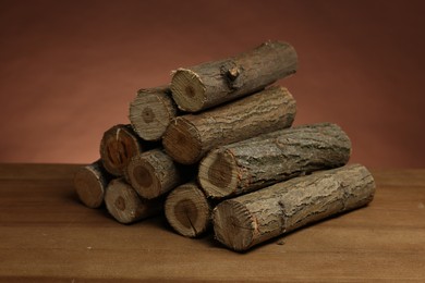 Photo of Pile of cut firewood on wooden table against brown background