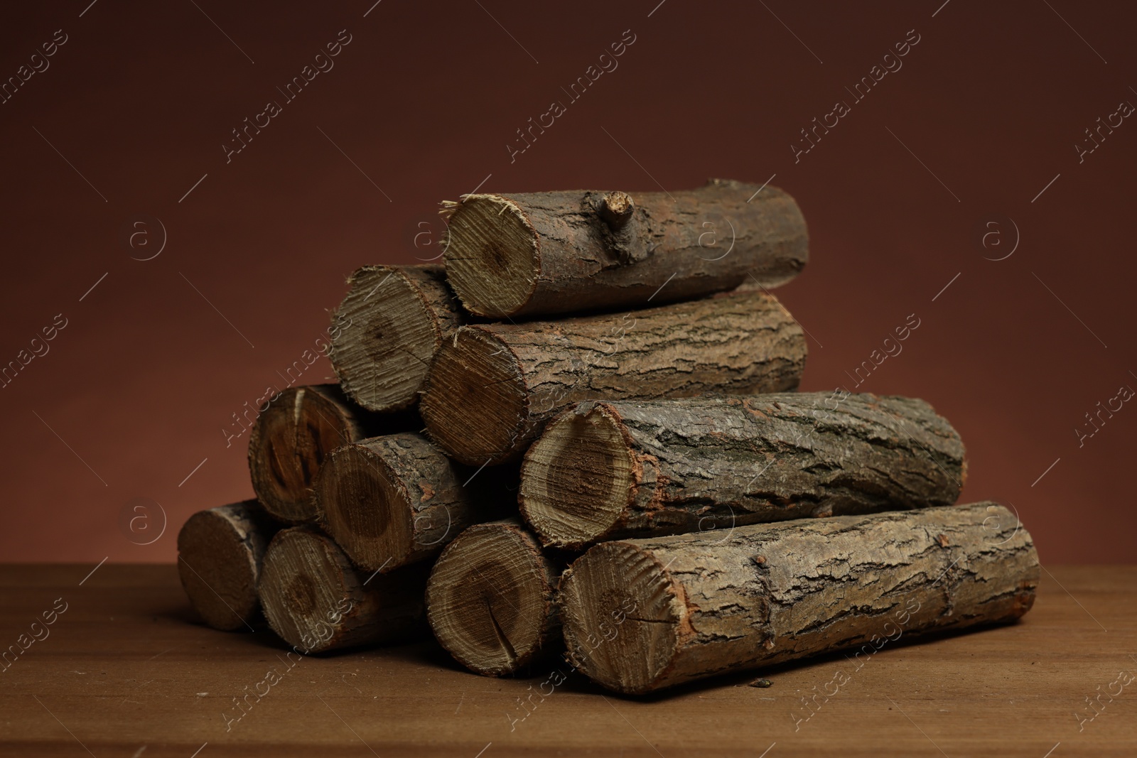 Photo of Pile of cut firewood on wooden table against brown background