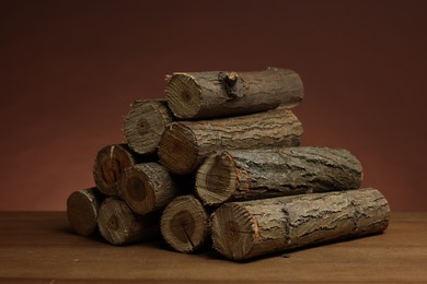 Photo of Pile of cut firewood on wooden table against brown background