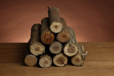 Photo of Pile of cut firewood on wooden table against brown background