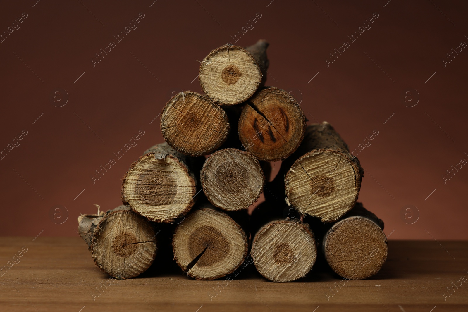 Photo of Pile of cut firewood on wooden table against brown background