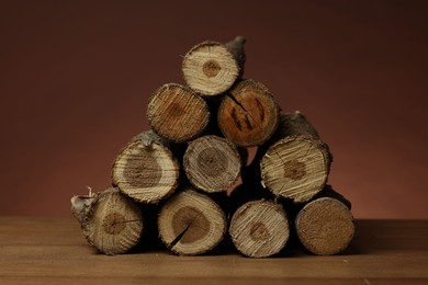 Photo of Pile of cut firewood on wooden table against brown background