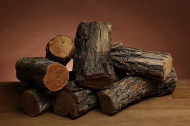 Photo of Pile of cut firewood on wooden table against brown background