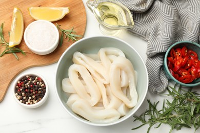 Photo of Uncooked squid rings and spices on white table, flat lay