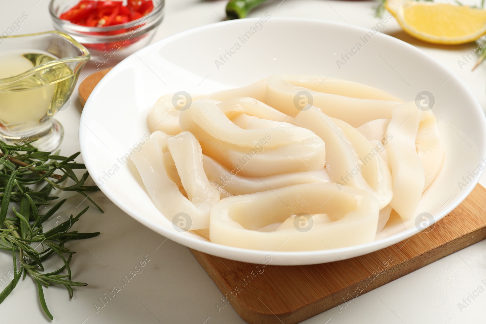Photo of Uncooked squid rings and spices on white table, closeup