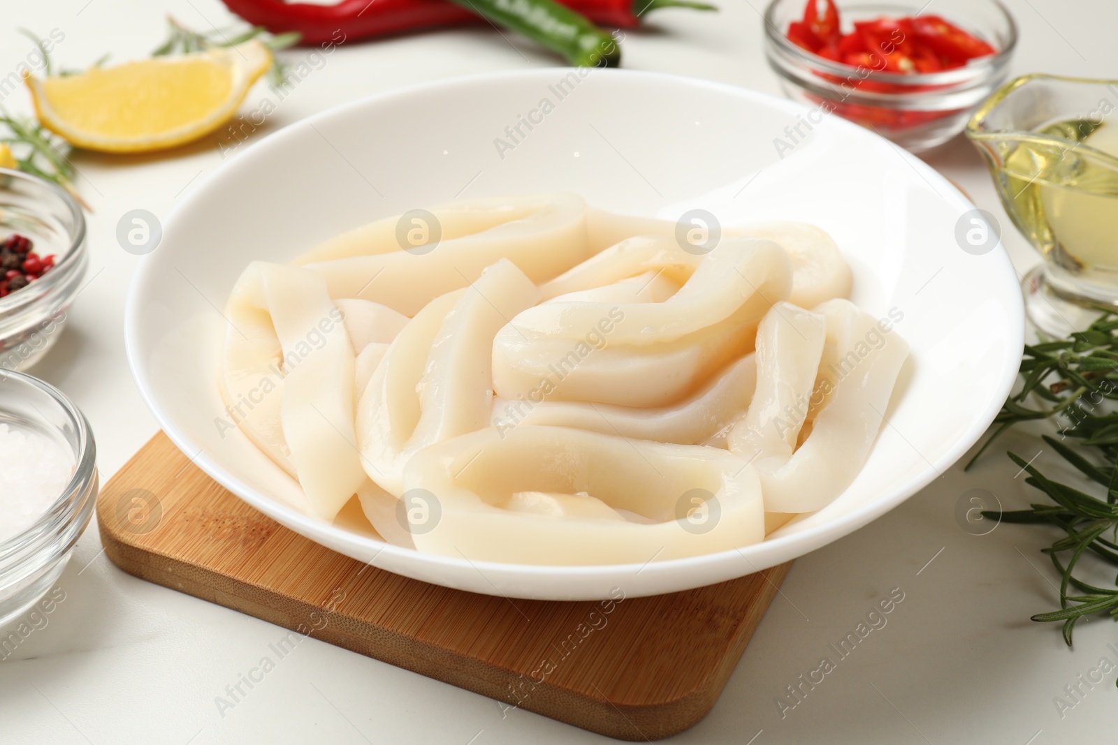 Photo of Uncooked squid rings and spices on white table, closeup