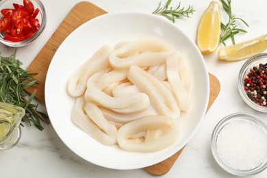 Photo of Uncooked squid rings and spices on white table, flat lay