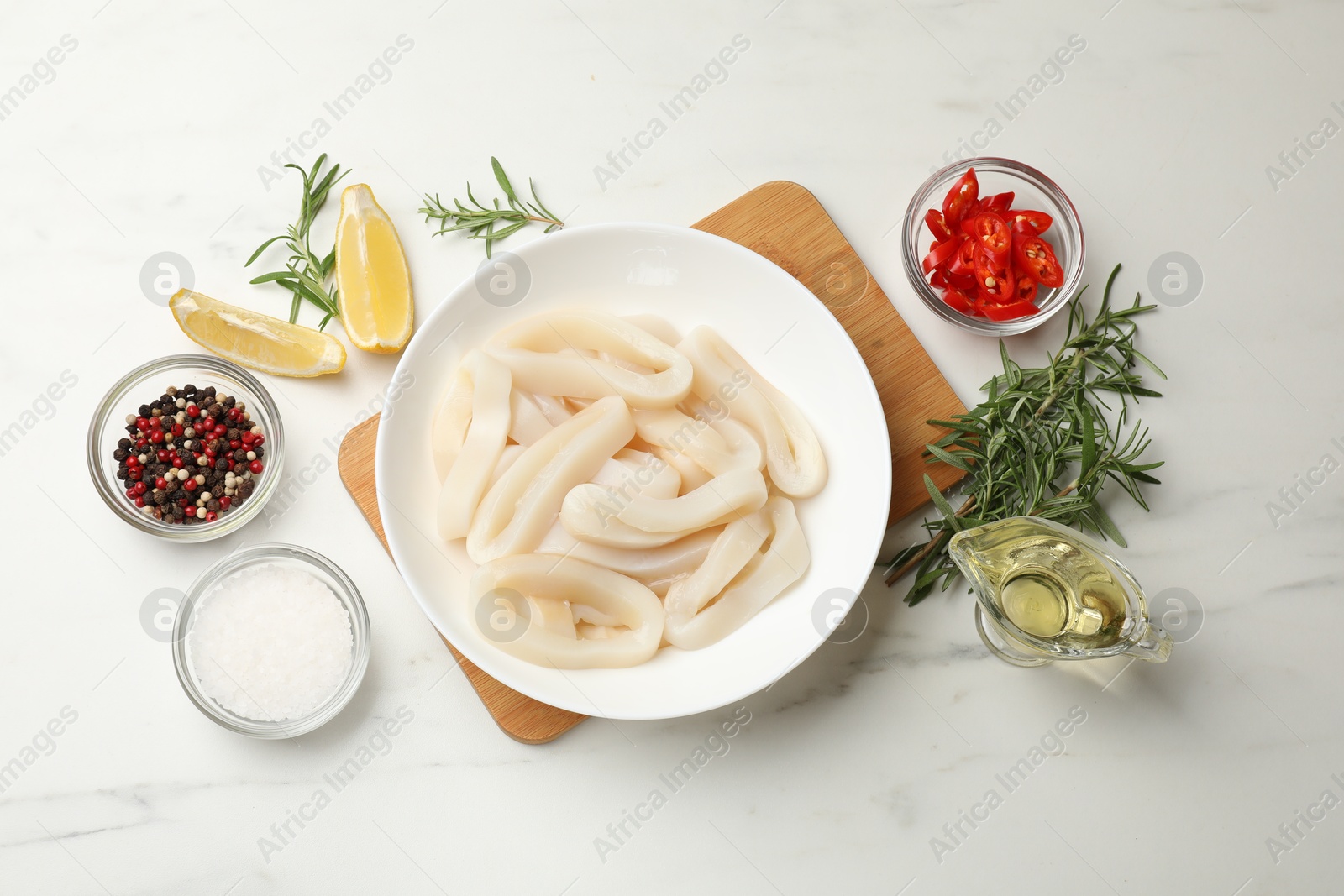 Photo of Uncooked squid rings and spices on white table, flat lay