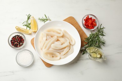 Photo of Uncooked squid rings and spices on white table, flat lay