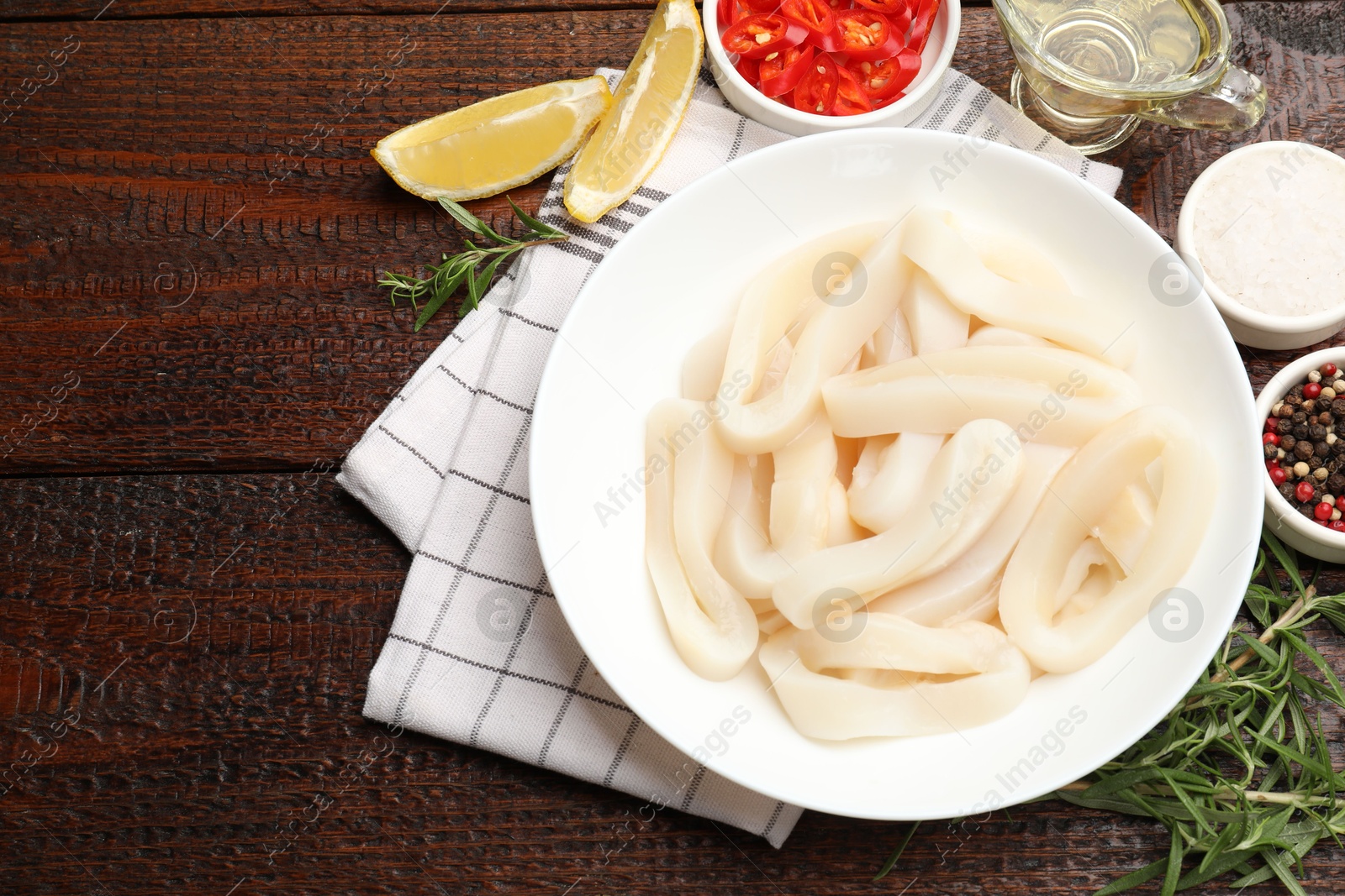 Photo of Uncooked squid rings and spices on wooden table, flat lay. Space for text