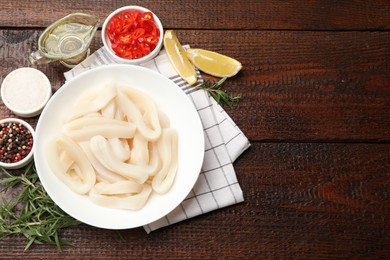 Photo of Uncooked squid rings and spices on wooden table, flat lay. Space for text